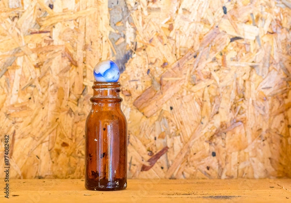 Fototapeta Closeup of Antique Amber Colored Bottle Topped with a Vintage Marble and a Particle Board Wood Background