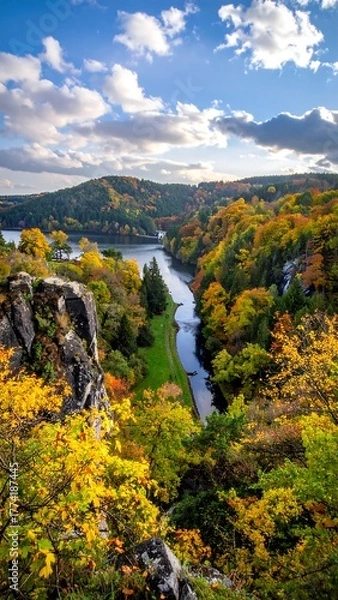 Fototapeta A river winding through forested hills, fall colors ablaze under a sunny, clouded sky