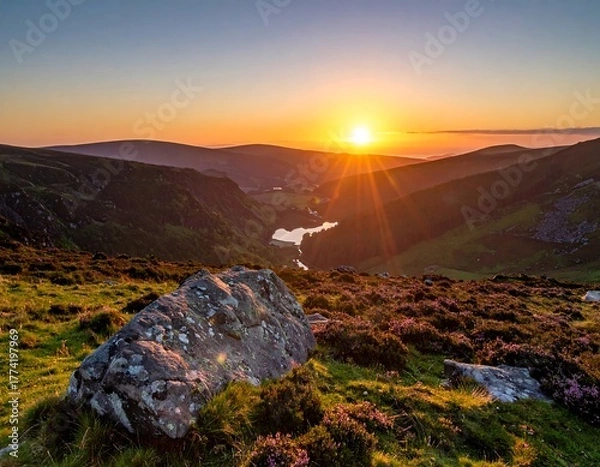 Fototapeta A breathtaking landscape photo captures a warm sunset casting golden rays over rolling hills and a tranquil lake nestled in the valley