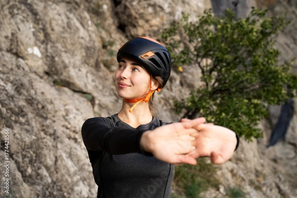 Fototapeta Young female athlete climber stretching hands before outdoor rock climbing, physical preparation and wellness in mountain environment
