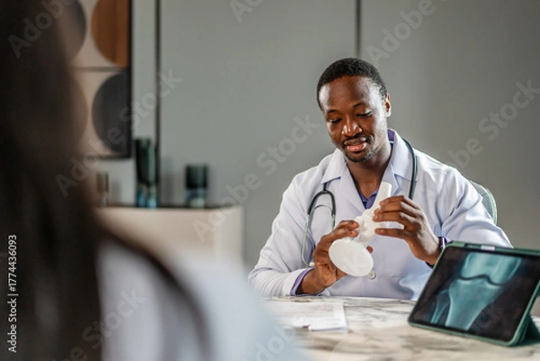 Fototapeta Cheerful doctor and young woman discuss her X-ray from a knee boneresults on a tablet computer. A man analyzes an MRI image to make a diagnosis for a patient, Female consulting trauma surgeon