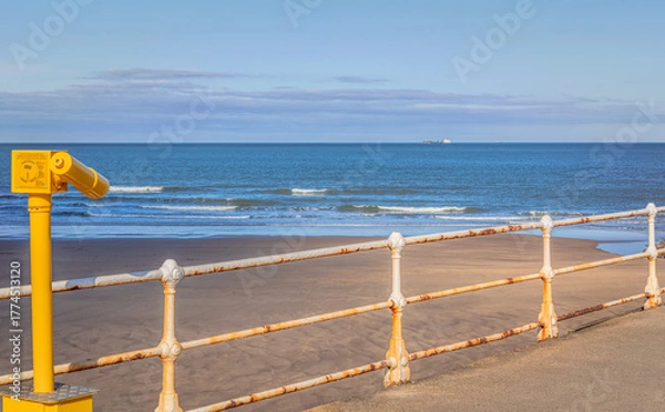 Fototapeta A pier with a telescope in the foreground and a ship on the horizon.