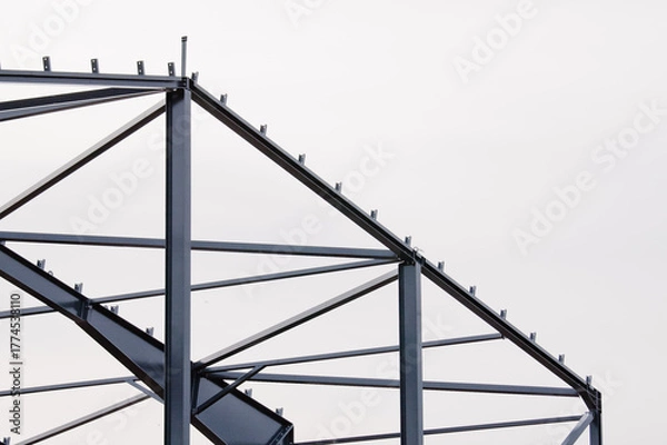 Obraz Metal construction, in the photo the structure of the building frame made of metal beams against the background of a gray sky