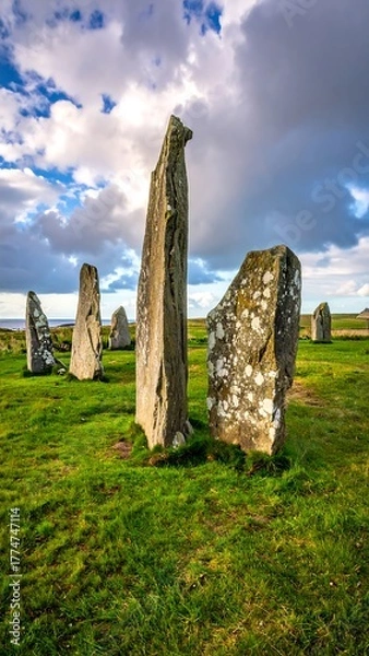Fototapeta Ancient stone circle standing tall on green grass beneath a cloudy, dramatic sky