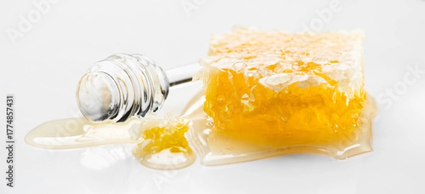 Obraz Fresh Honey in honeycombs dripping, pouring from a glass honey dipper spoon, on white background. Honeycomb close-up. Healthy organic liquid honey spill. 