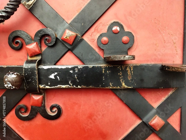 Fototapeta Old forged black iron latch with rivets on red wooden door, vintage metalwork detail, rustic architecture close-up
