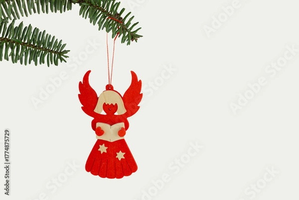 Fototapeta red wooden Christmas angel ornament with stars hanging from a pine branch on a white background
