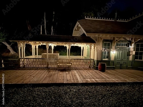 Obraz Vintage Train Station at Night: A nostalgic depot with a wooden walkway, illuminated by warm lights under a dark sky, evoking history.