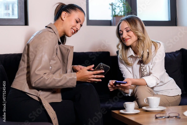 Fototapeta Two friends enjoy a casual conversation while looking at their phones in a cozy cafe