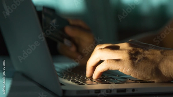 Fototapeta The concept of credit card theft. Hackers with credit cards on laptops use these data for unauthorized shopping. Unauthorized payments from credit card owners. In the hacker's secret office