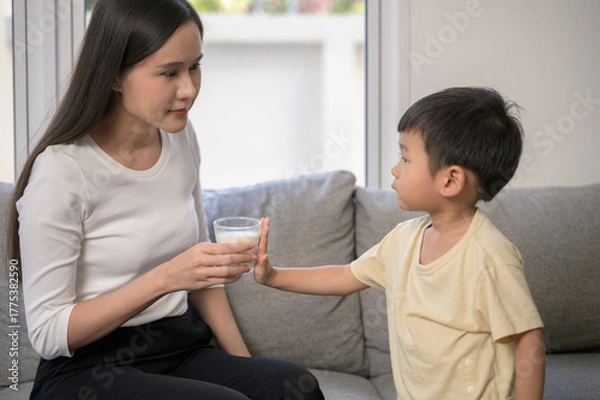 Fototapeta Adorable Asian baby boy using hand refuse drinking cow milk from his mother showing lack of appetite or picky eating behavior. Concept of child nutrition, food refusal, and parenting challenges.
