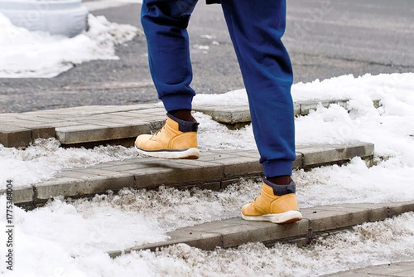 Fototapeta Man in warm boots moving slowly on snowy outdoor steps, safety awareness during cold winter weather, icy conditions. Snowy staircase with man in winter footwear maintaining balance to avoid slipping