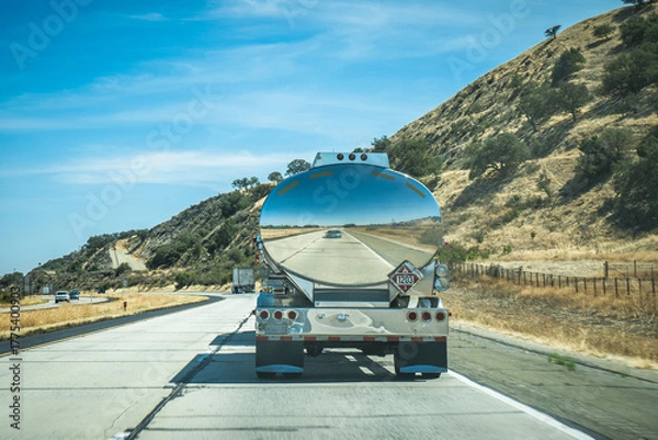 Fototapeta Fuel tanker truck driving on California highway through dry hills, bright sunny day, mirror reflection of the road in the shiny metal tank, travel and transportation scene, perspective view, minimalis