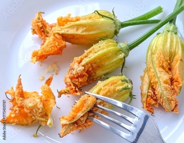 Fototapeta Several deep-fried zucchini flowers on a white plate. A fork is partially visible, indicating someone is about to eat one.