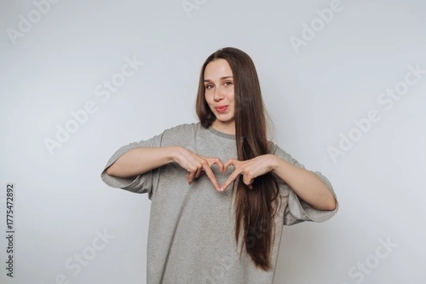 Fototapeta Young woman making a heart shape with her hands against a plain background.