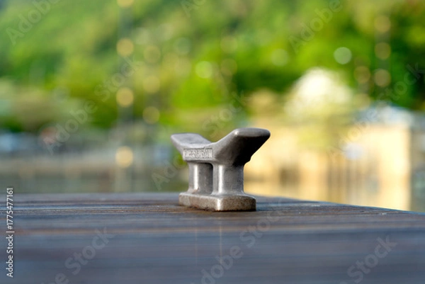 Fototapeta Metal Mooring Cleat on a Wooden Dock, Aged and Weathered, Set Against a Blurred Green Background with Soft Bokeh Lights