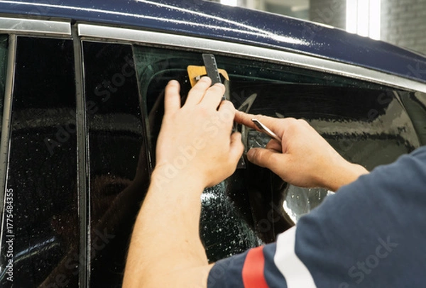 Obraz Male car service worker glue window tinting in luxury car detailing car repair the concept of love for cars and protection. Applying tinting foil on a car window in the tuning studio close-up. 