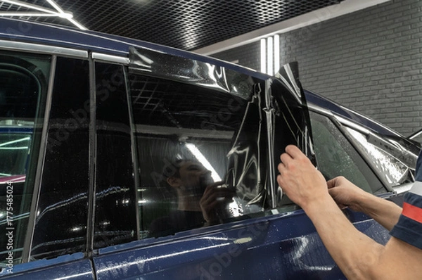 Fototapeta Male car service worker glue window tinting in luxury car detailing car repair the concept of love for cars and protection. Applying tinting foil on a car window in the tuning studio close-up. 