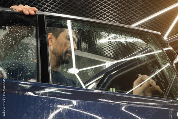 Fototapeta Male car service worker glue window tinting in luxury car detailing car repair the concept of love for cars and protection. Applying tinting foil on a car window in the tuning studio close-up. 