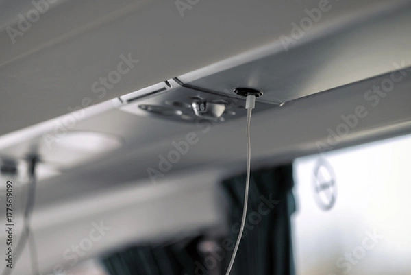 Obraz A close-up shows a white charging cable plugged into a black USB port located in the overhead panel of a modern coach bus, highlighting passenger technology.