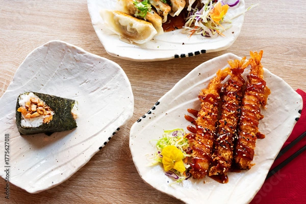 Fototapeta Japanese traditional snacks, prawn tempura, onigiri and gyoza served on white plates.