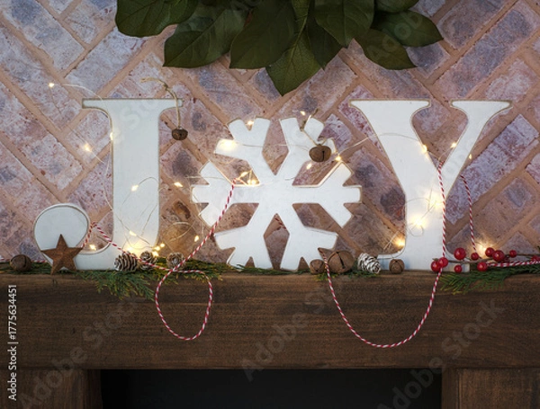 Obraz Brick fireplace hearth mantle Christmas holiday festive decoration with white JOY block farmhouse word letters and fairy lights, green wreath and brown wood shelf.
