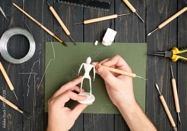 Fototapeta Craftsman hands working on human sculpture, sculpturing from polymer clay against working table with tools. Flat lay, top view