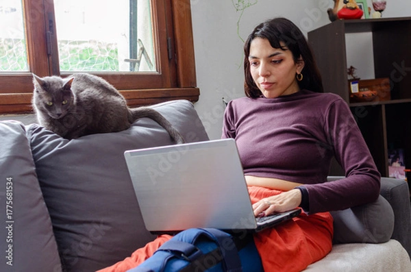 Fototapeta Young disabled woman using her laptop laying on the couch.