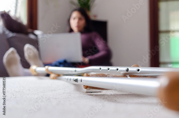 Fototapeta Crunch foreground photo with a young disabled woman using her laptop laying on the couch on background.