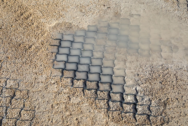 Obraz Polymer geogrid with gravel fill showing soil stabilization under wet conditions. For erosion control, permeable pavement, and road construction projects. Real photo