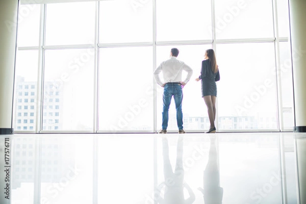Fototapeta Office staff is discussing something by the window standing with their backs