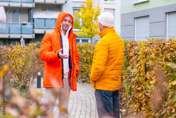 Fototapeta Two men chatting on paved autumn path near modern apartment buildings, arguing on a city street, emotional conversation, relationship tension, Generational dialogue outdoors, Autumn emotions