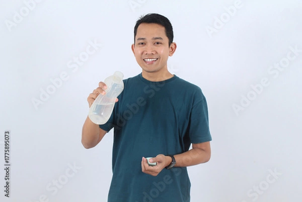Obraz Smiling Asian man holding reusable water bottle for healthy hydration
