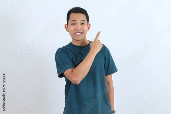 Obraz Happy Asian man pointing finger up to blank copy space