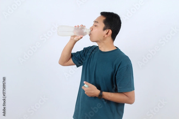 Obraz Thirsty Asian man drinking water from reusable bottle for hydration