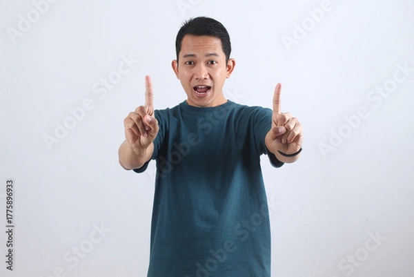 Obraz Excited Asian man pointing fingers up making number one gesture