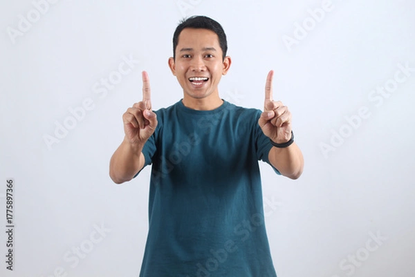 Obraz Happy excited Asian man pointing fingers up isolated on white background