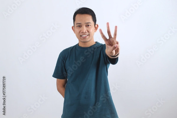 Obraz Smiling Asian man showing three fingers counting gesture