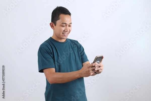 Obraz Smiling Asian man using smartphone against white background