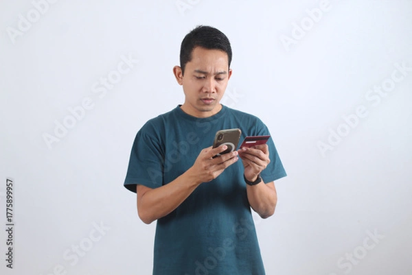 Obraz Asian man paying online with credit card and smartphone on white background.
