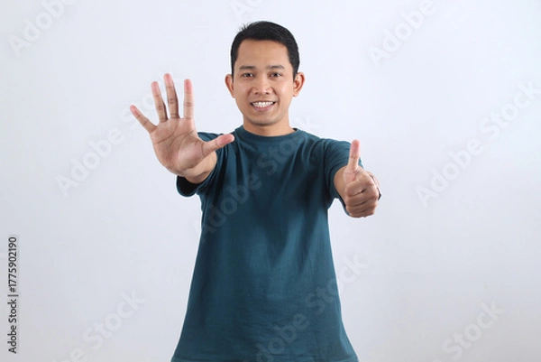 Obraz Happy Asian man showing number six with fingers and thumbs up gesture