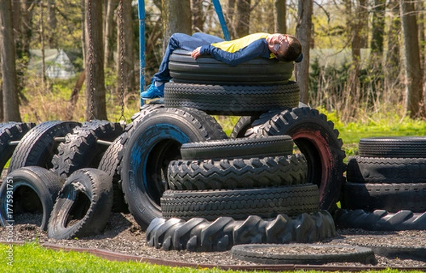 Obraz Boy lies  on top of a tire tower, a recycled play structure on a rural play ground 