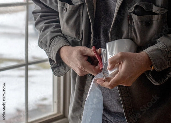 Obraz cutting plastic for window insulation with a scissors, used to help keep heat in a home during winter time 