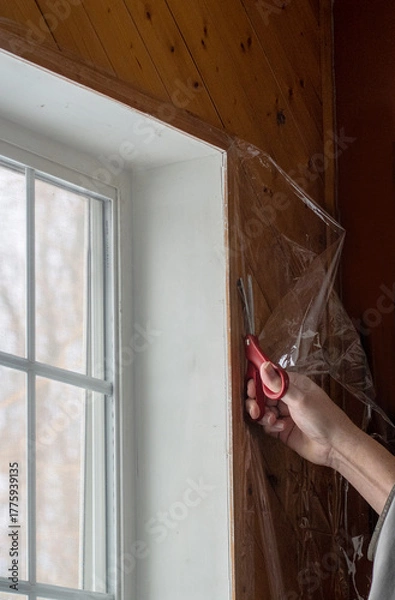 Fototapeta  a hand holding scissors is Trimming window  plastic, used for window insulation and saving on the heating bill in winter 