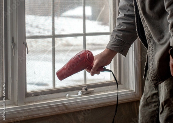 Obraz  A hand holds a blow dryer and is being used to Shrink wrap a window, to help insulate and keep in the heat for winter