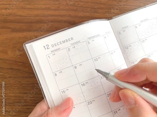 Fototapeta A woman's hands filling out a December schedule book on a wooden table