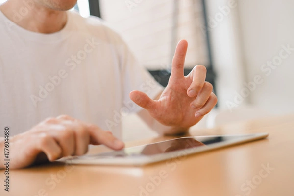 Fototapeta man interacting with a digital tablet on a wooden table, illustrating modern technology usage, user interface gesture control touch screen behavior in a bright indoor space.