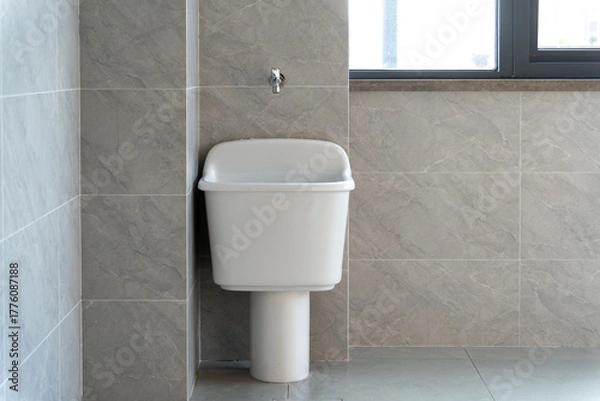 Obraz white mop sink with a faucet, set against gray marble tiles, near a bright window