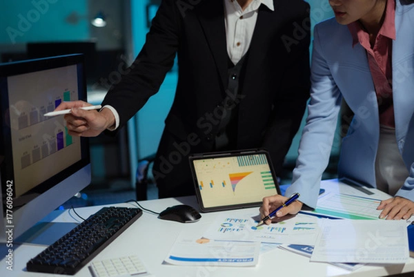 Obraz Financial analysts work overtime analyzing data on tablets, laptops, and graphs.