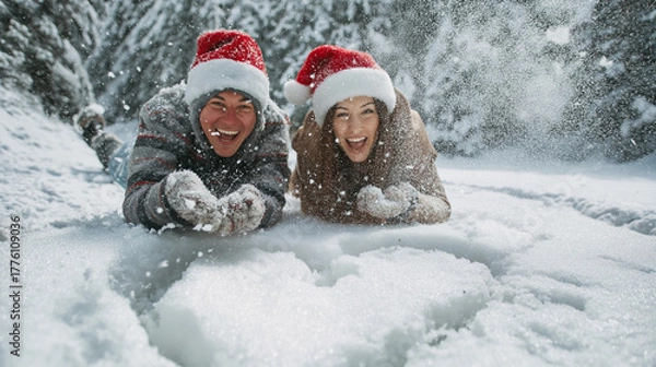 Obraz Playful couple wearing Santa hats having snowball fight around heart shape drawn in snow, laughing joyfully, snow flying in air, heart symbol between them, dynamic action shot, winter forest setting